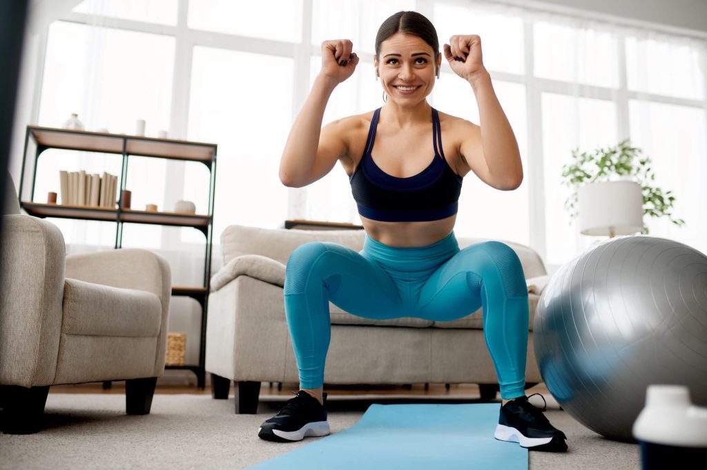 Woman performing squats on exercise mat at home with stability ball and fitness equipment in living room